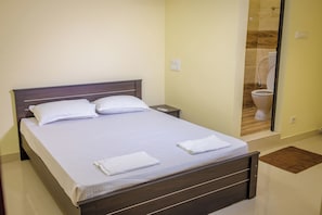 Una cama bien hecha con sábanas y almohadas blancas, un cabecero de madera y una mesita de noche con una lámpara.