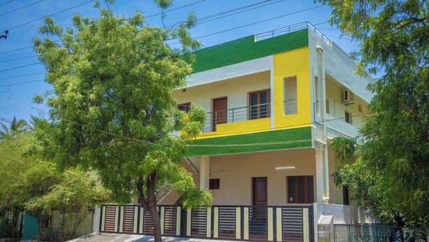 A two-story building with a green and yellow facade, a gated entrance, and a tree in the foreground.