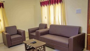 A living room with a brown sofa, two armchairs, and a small wooden coffee table with a remote control.