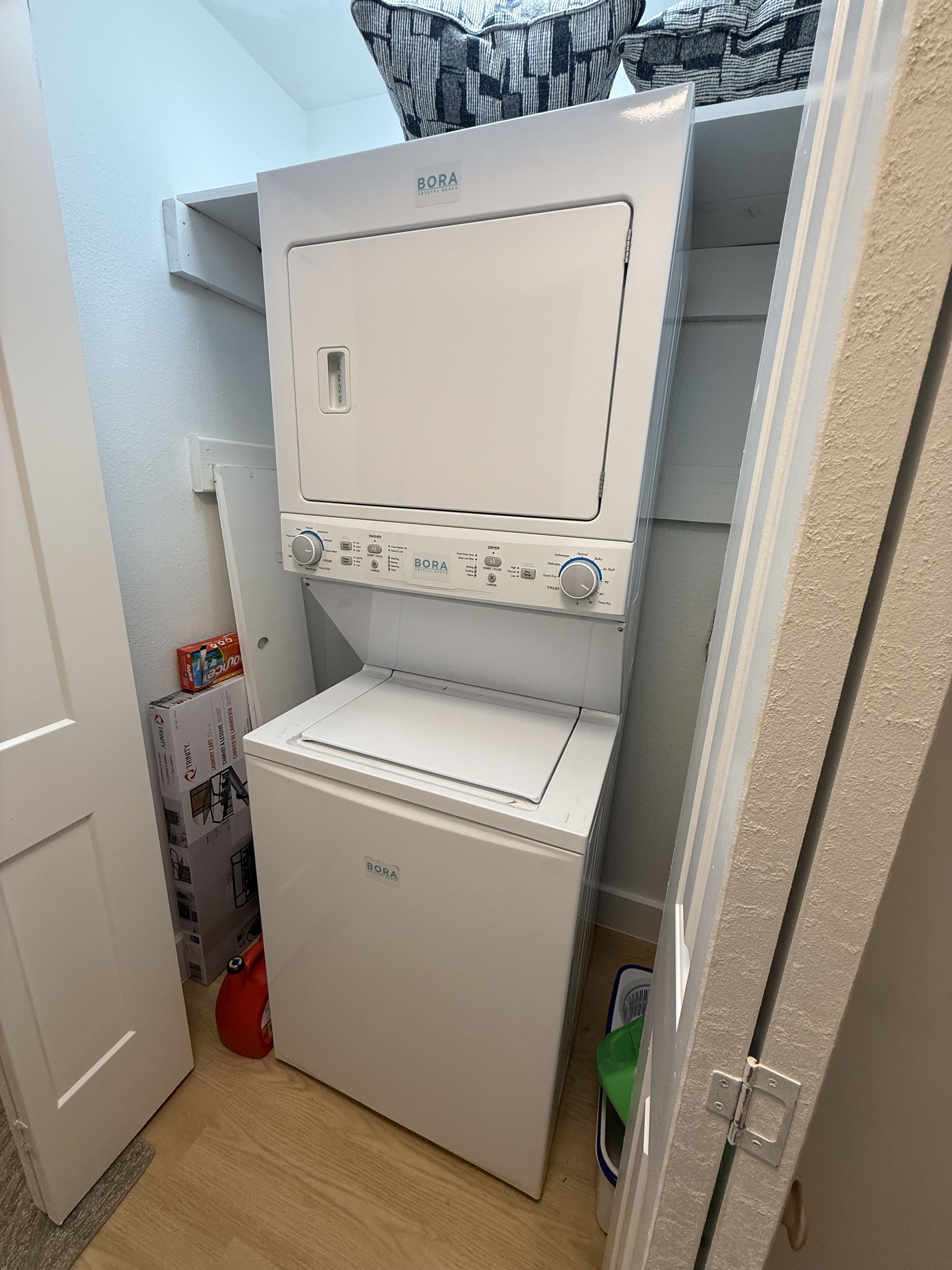 A compact, white BORA washing machine and dryer unit in a small laundry room with a wooden floor and a white door.