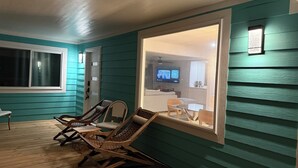 A room with teal walls, a wooden floor, and a large window. There are two wooden chairs and a small table. A television is visible through the window. - AZURE beach villa at Galveston  (Galveston)