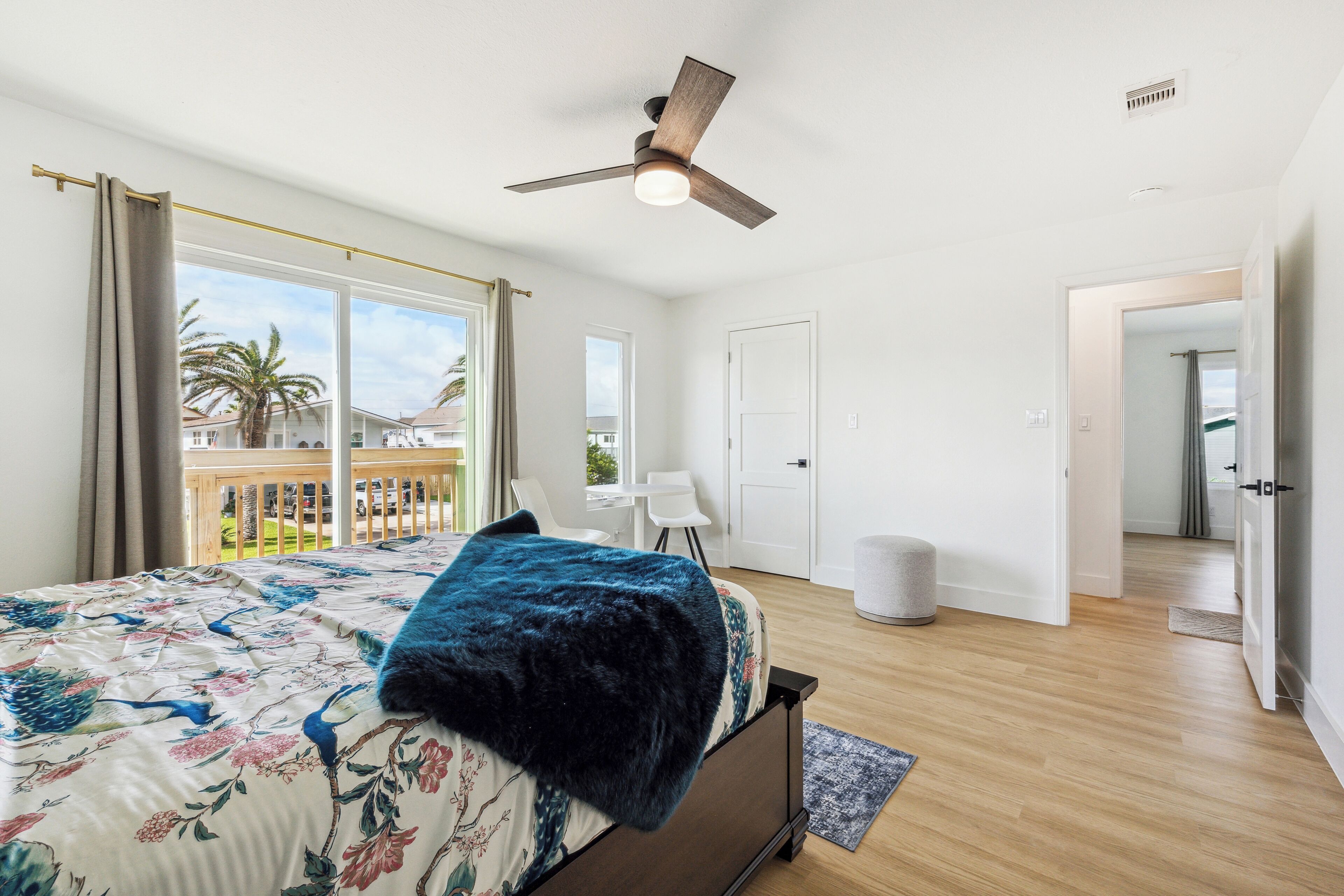 A bedroom with a bed, a ceiling fan, a window with curtains, and a view of a balcony.