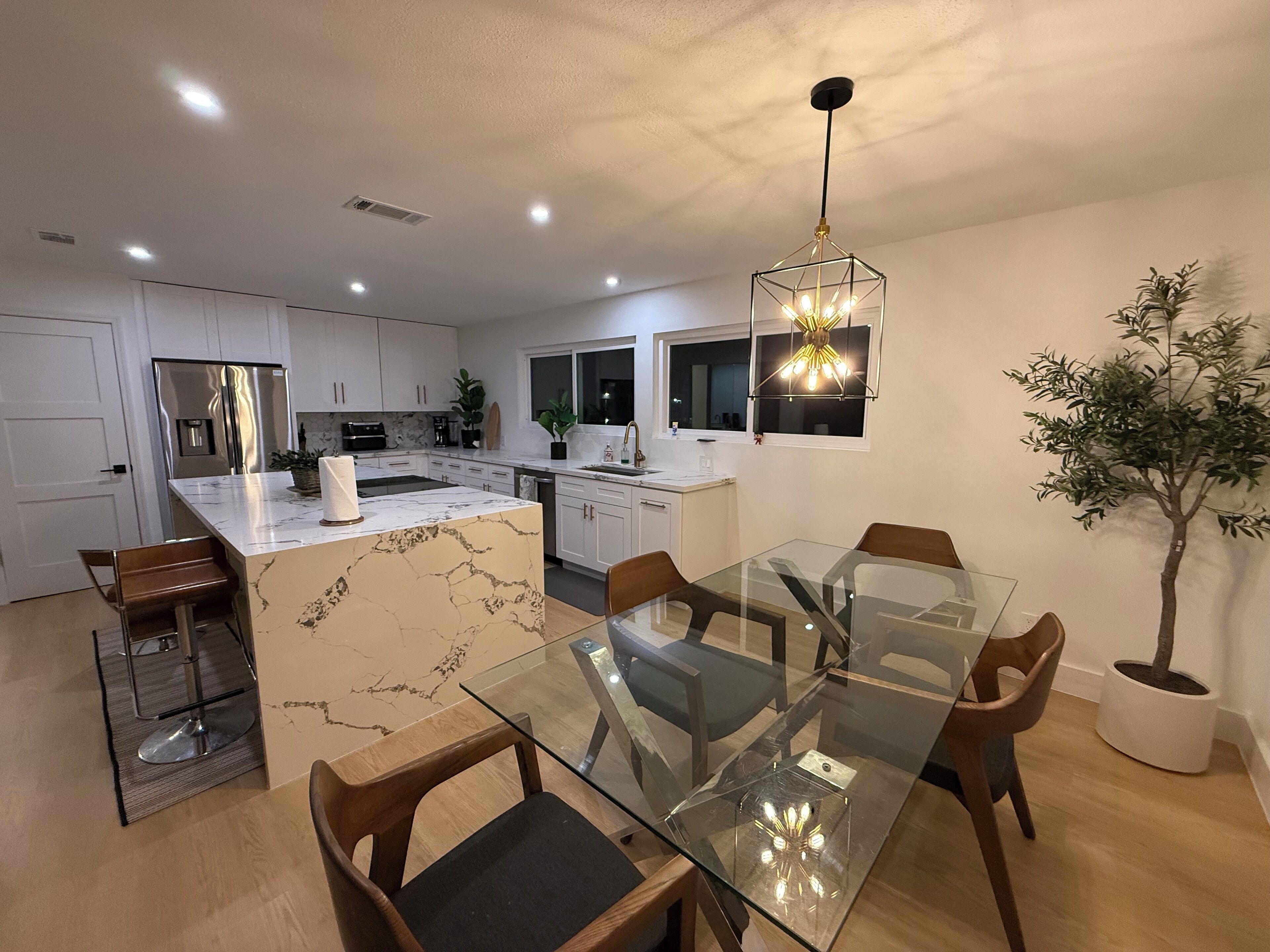 Een moderne keuken met witte kasten, een centraal eiland en een eethoek met een glazen tafel en houten stoelen.