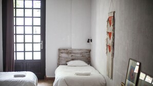 Una habitación con dos camas, un cabecero de madera, una mesita y una puerta con ventana.
