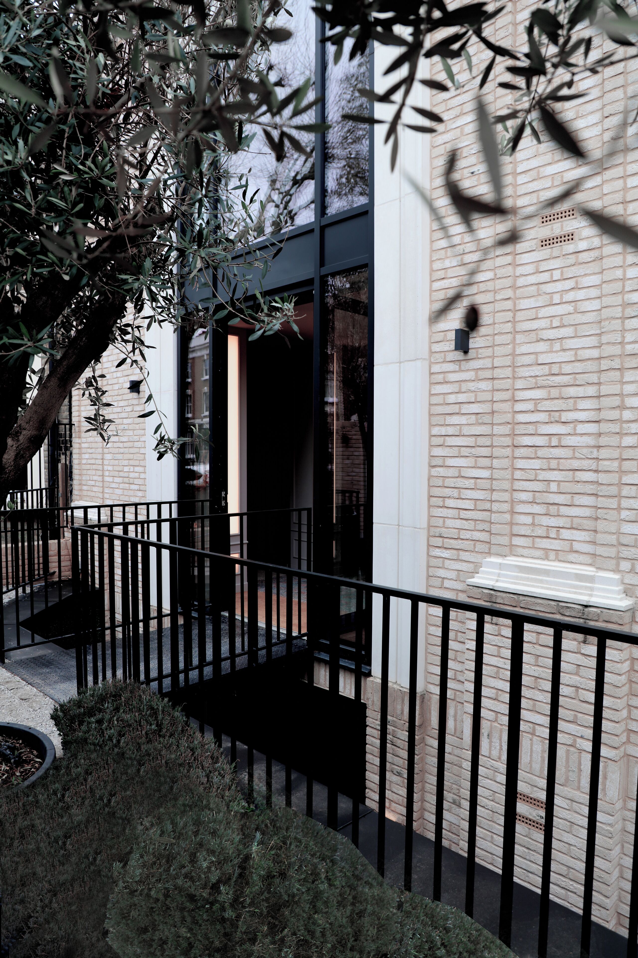 A modern building with a brick facade, a black metal railing, and a tree in the foreground.