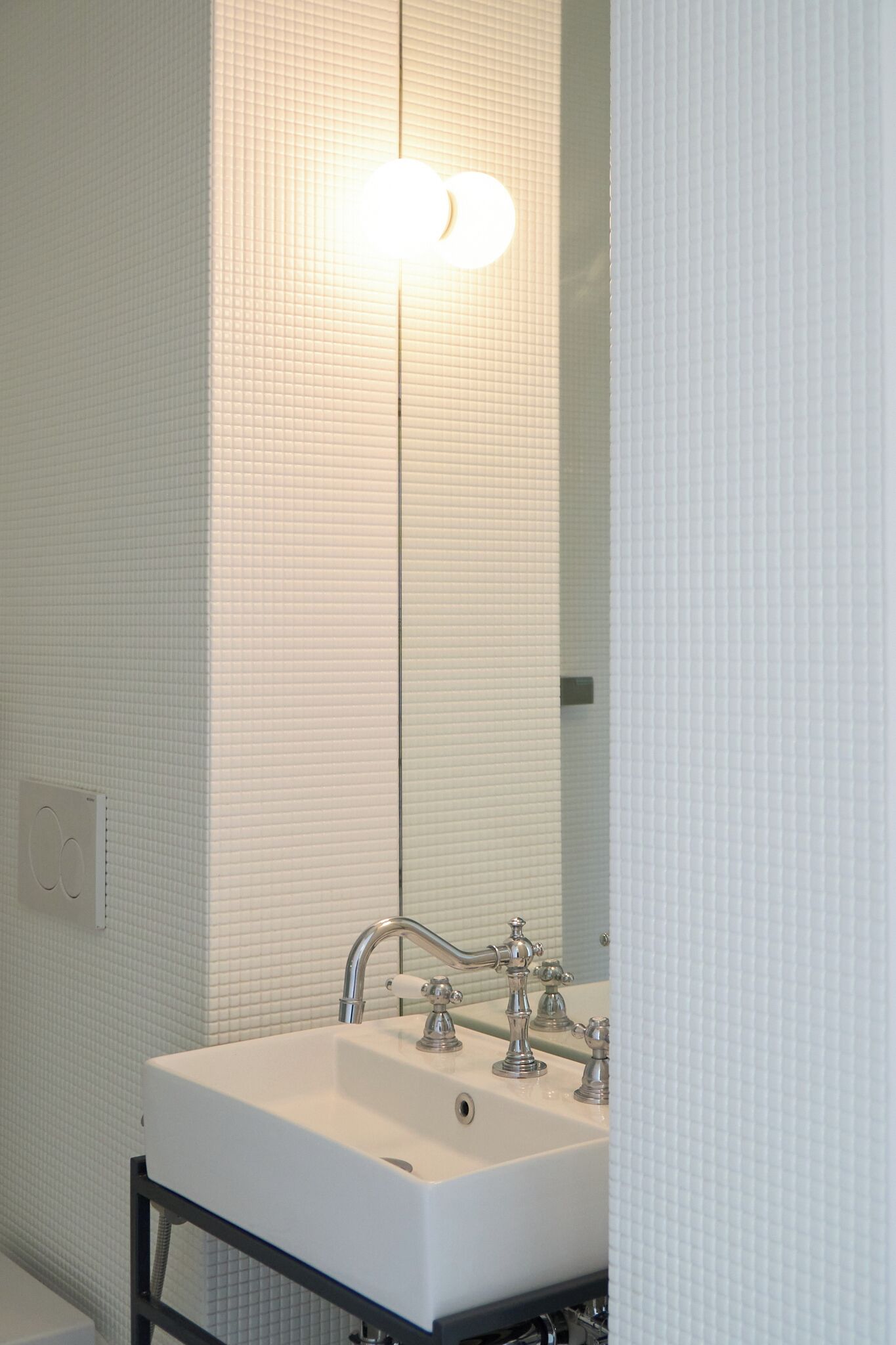 A bathroom with a white sink, a mirror, and a light fixture above the mirror.