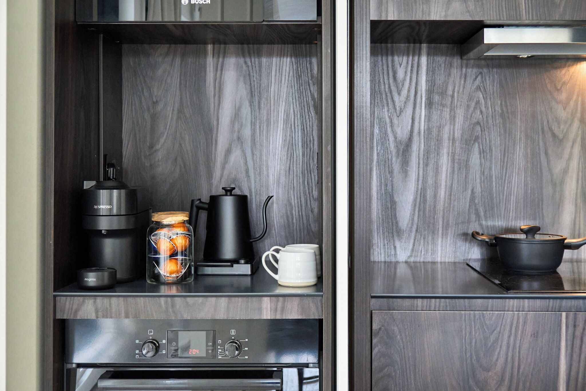 A kitchenette with a coffee maker, a jar of oranges, and a white mug on the counter.
