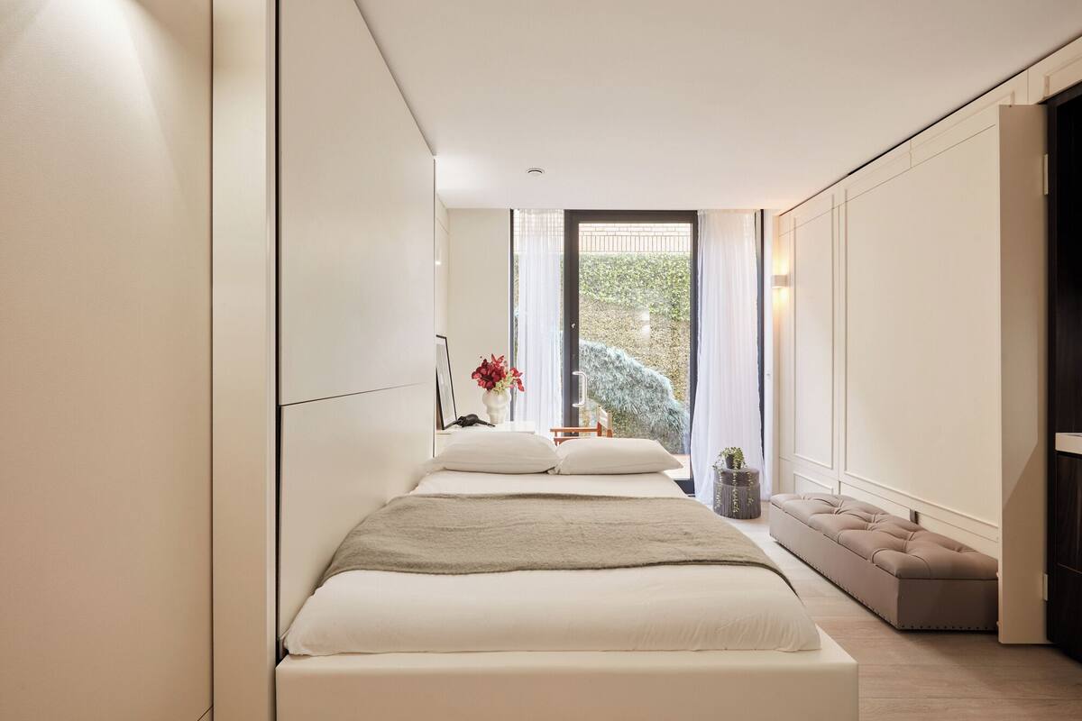 Ein modernes Schlafzimmer mit einem großen Bett, einem Nachttisch und Blick auf Grünfläche draußen.