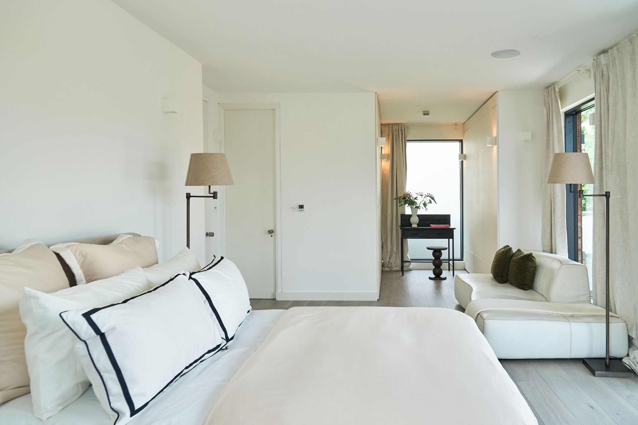 A hotel room with a large bed, a sofa, a desk, and a lamp.