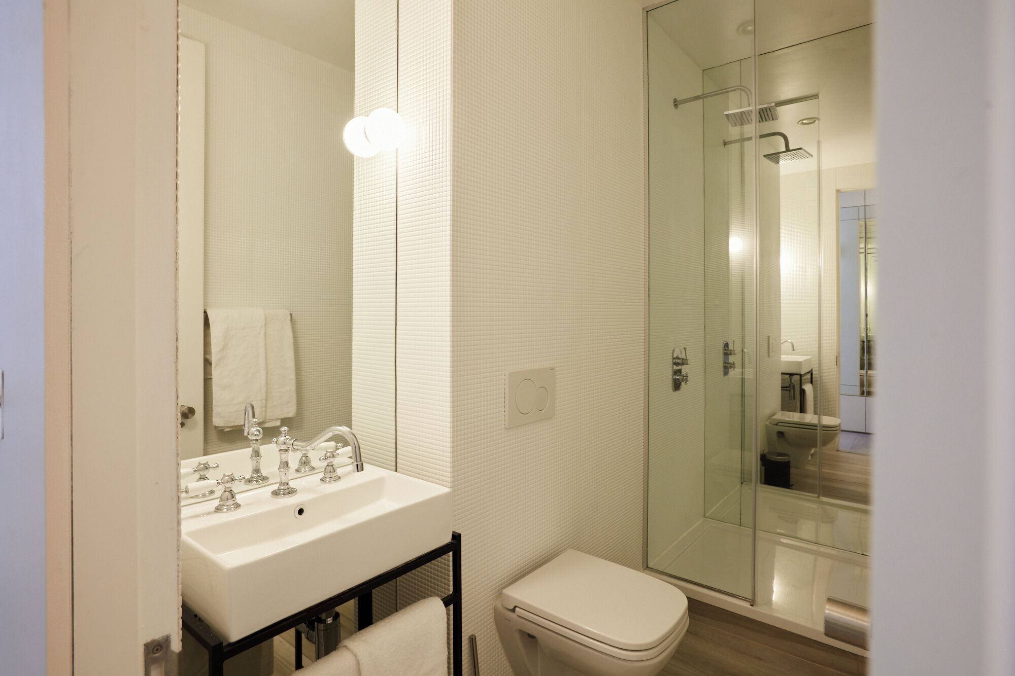 A modern bathroom with a glass-enclosed shower, a white sink with multiple faucets, and a toilet.