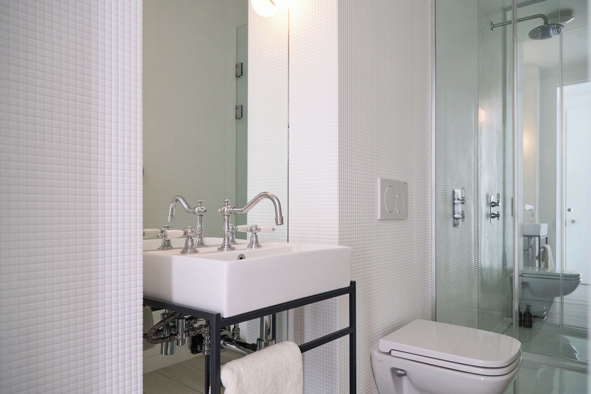 A modern bathroom with a white sink, two faucets, a glass shower enclosure, and a toilet.