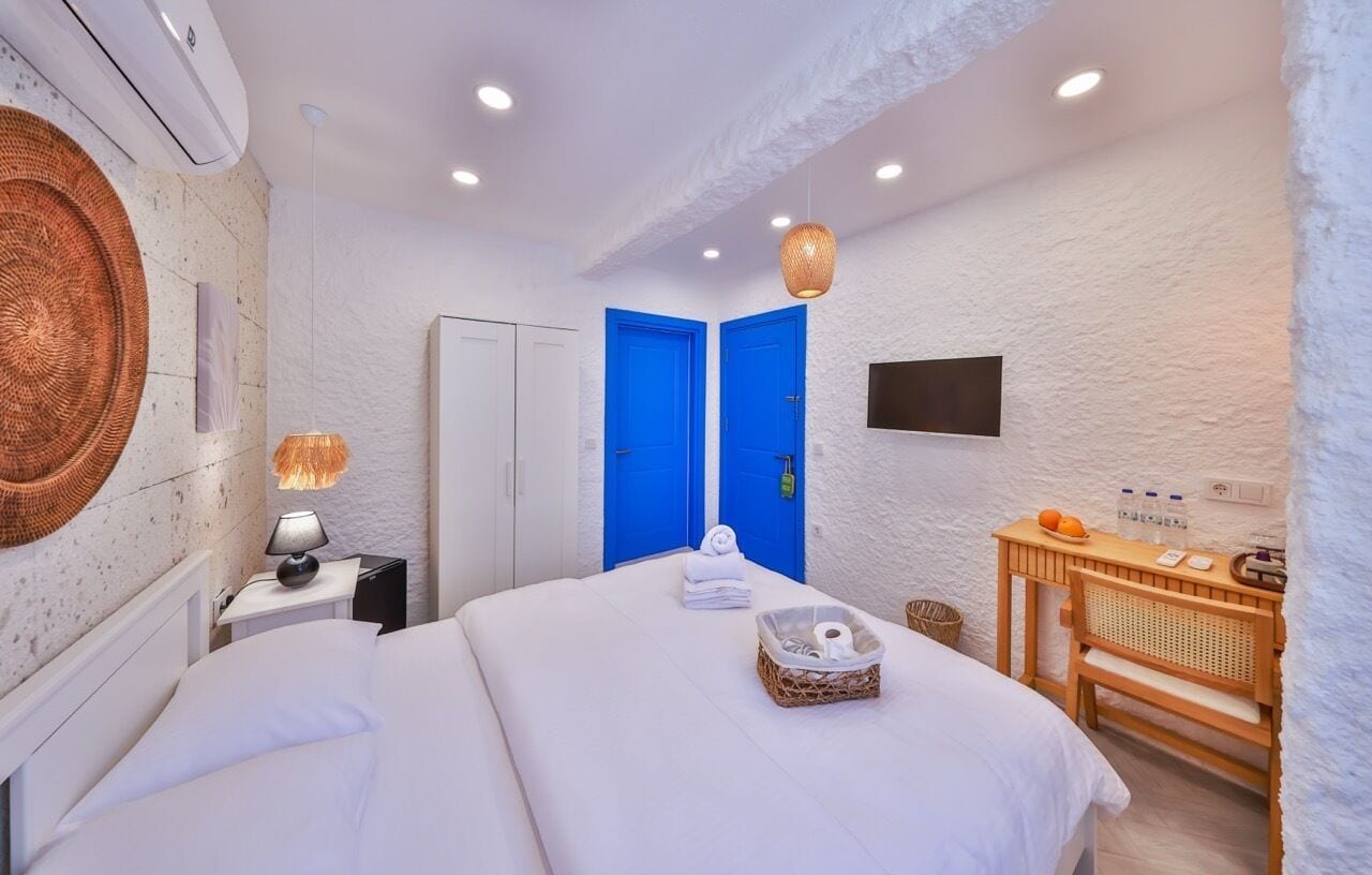A hotel room with a bed, a desk with a lamp, a TV, and a wall-mounted air conditioner.