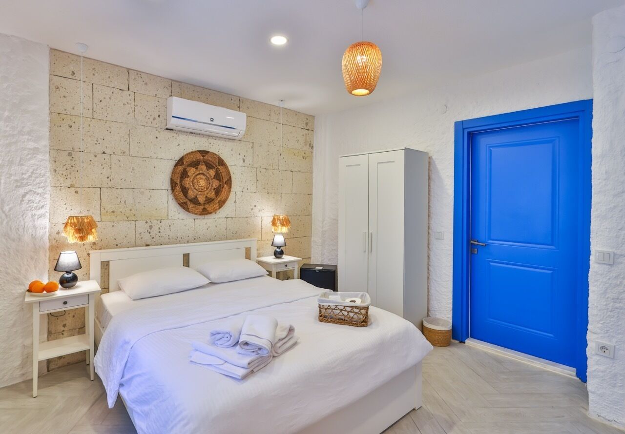A hotel room with a large bed, a wardrobe, a blue door, and a wall-mounted air conditioner.