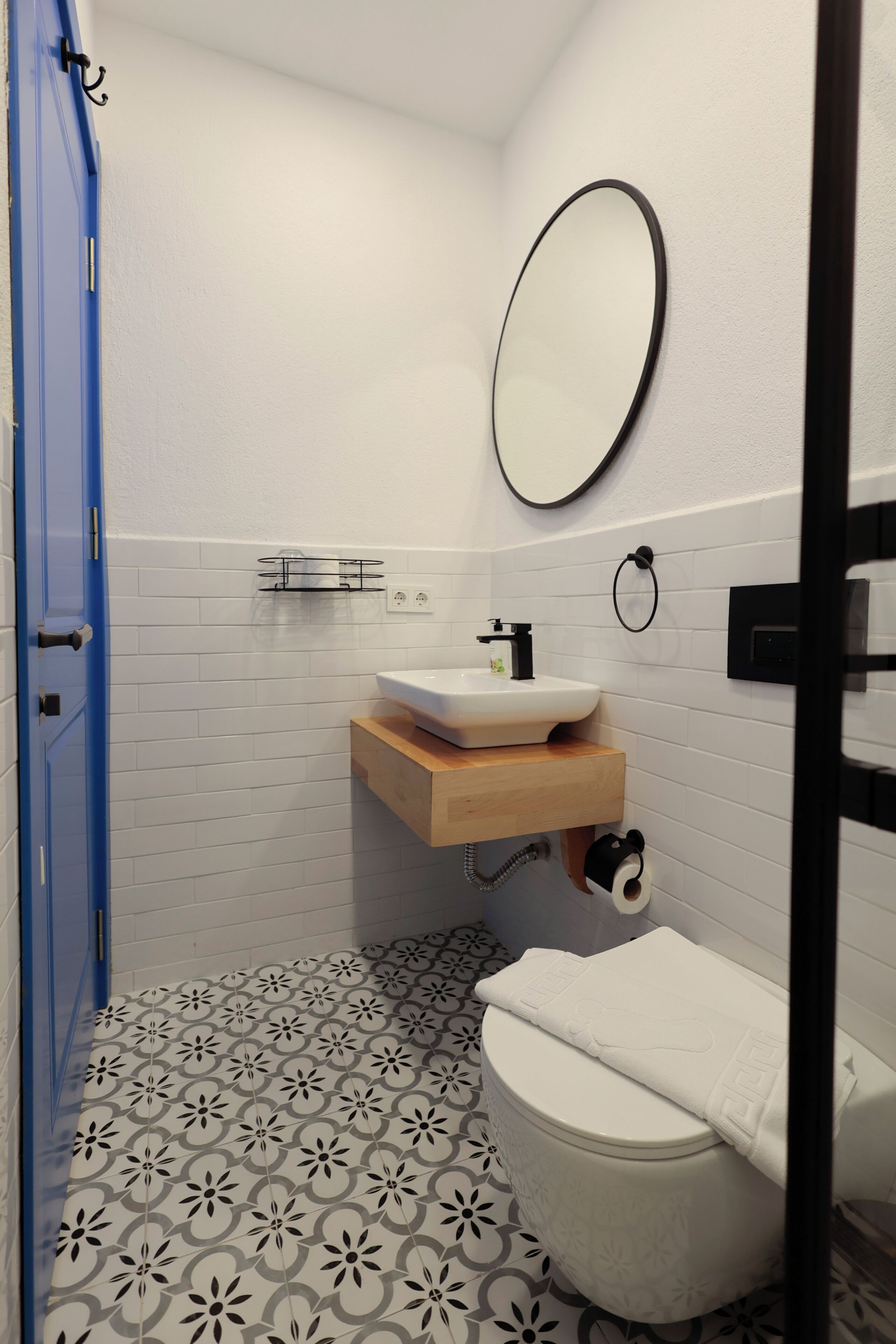 A bathroom with a toilet, sink, mirror, and patterned floor tiles.