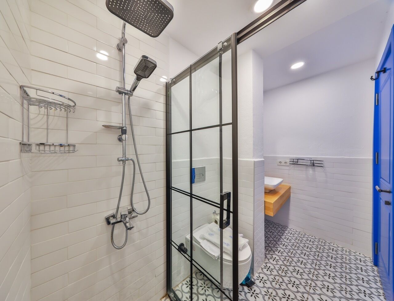 Een moderne badkamer met een douchecabine van glas, witte betegelde wanden, een vloer met patroon en een blauwe deur.
