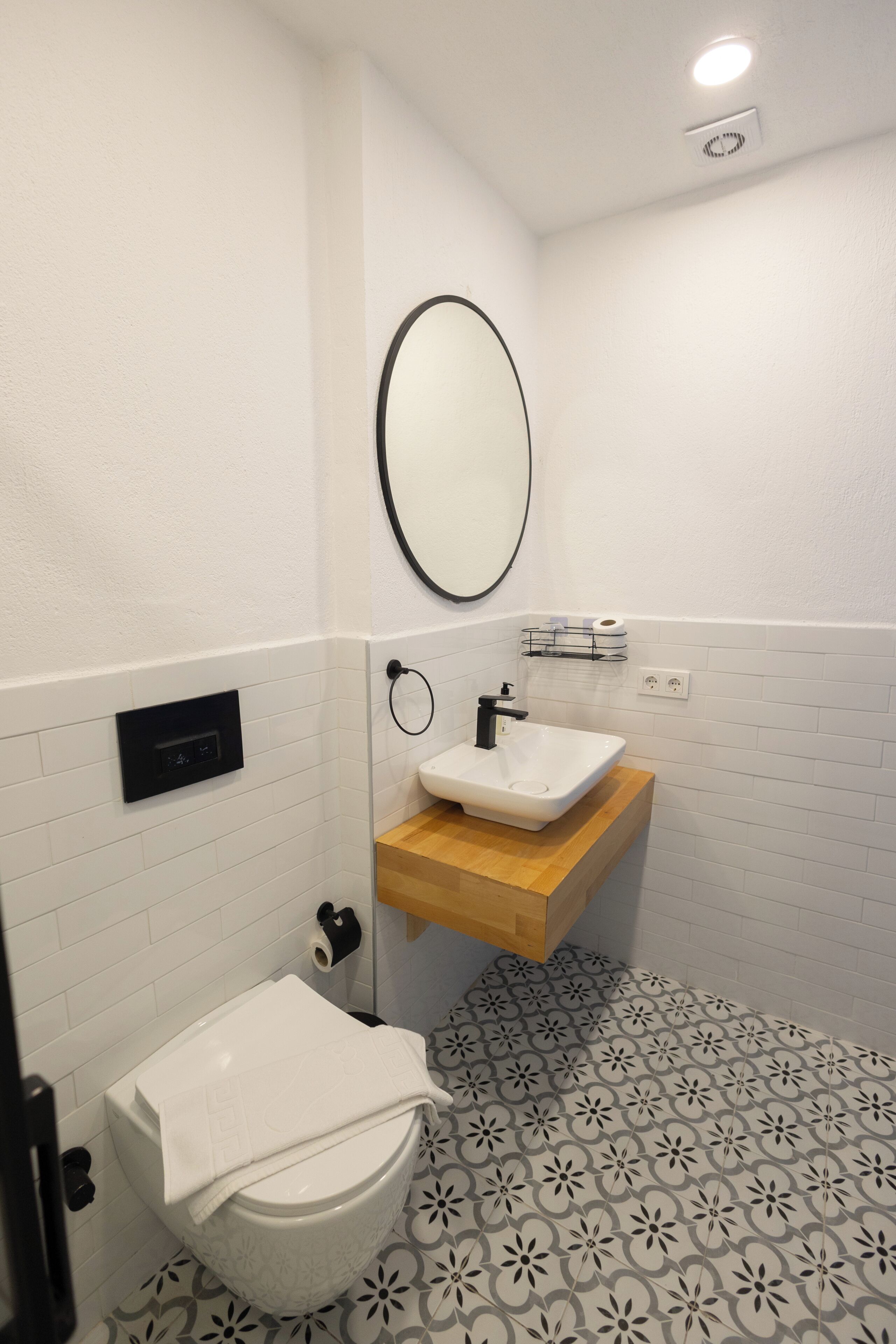 A bathroom with a white toilet, a sink with a wooden countertop, a mirror, and patterned floor tiles.