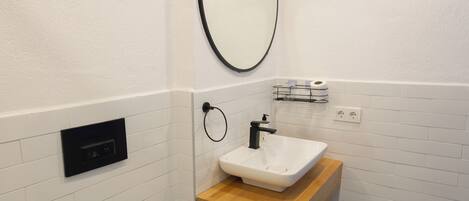 A bathroom with a white toilet, a sink with a wooden countertop, a mirror, and patterned floor tiles.