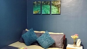 Een slaapkamer met een bed, kussens, een nachtkastje, een vaas met bloemen en drie ingelijste foto's aan de muur.