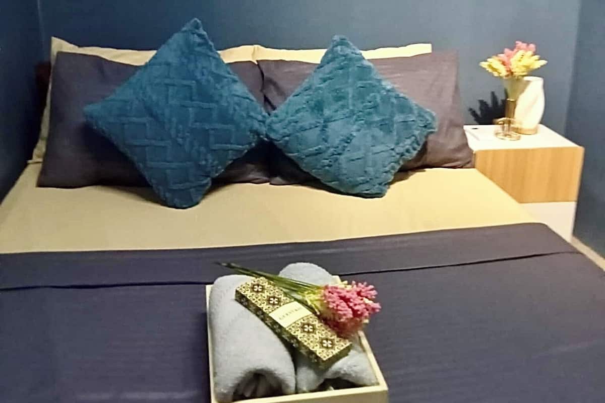 Una cama con dos almohadas, una mesita de noche con un florero y tres cuadros en la pared.
