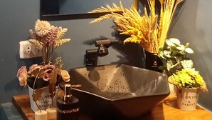 Een badkamer wastafel met een spiegel, een wastafel en diverse decoratieve items, waaronder gedroogde bloemen en een fles.