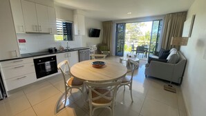 Una cocina moderna con armarios blancos, un comedor con una mesa redonda y sillas, y una sala de estar con un sofá y televisor.