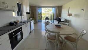 Una cocina moderna con armarios blancos, encimera negra y una zona de comedor con una mesa redonda y sillas blancas.