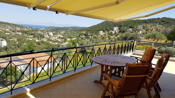 Un balcon avec une table et des chaises, offrant une vue sur une ville située sur une colline et sur les montagnes.