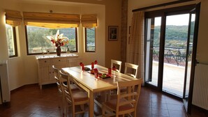 Un coin repas avec une table et des chaises en bois, un vase de fleurs et une vue sur un balcon doté d’une balustrade.