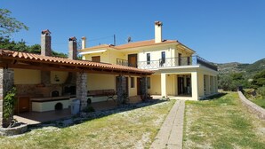 Une maison à deux étages avec une cheminée en pierre, un balcon et un chemin en pierre menant à l’entrée.