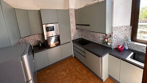 A compact kitchen with grey cabinets, a built-in oven, a microwave, and a window with a view.