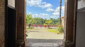 Une entrée en arc donnant sur une cour intérieure, avec un chemin de gravier, des plantes en pot et des chaises rouges.
