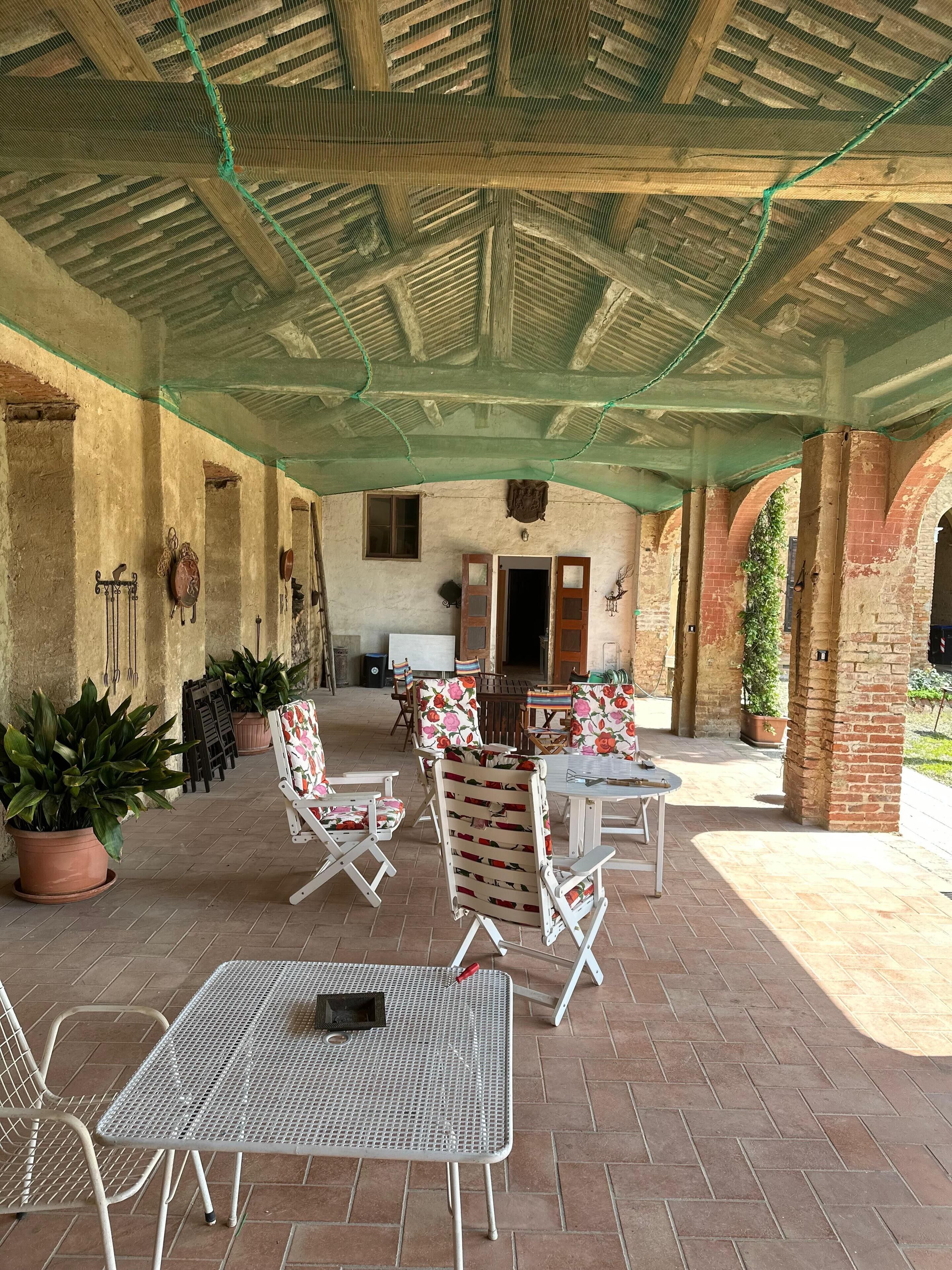 An outdoor patio area with brick flooring, white metal tables and chairs, and potted plants.