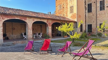 A courtyard with three striped lounge chairs, a brick building with arches, and a small tree.