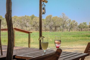 A wooden table with two glasses of wine, a lantern, and a view of a grassy field with trees.
