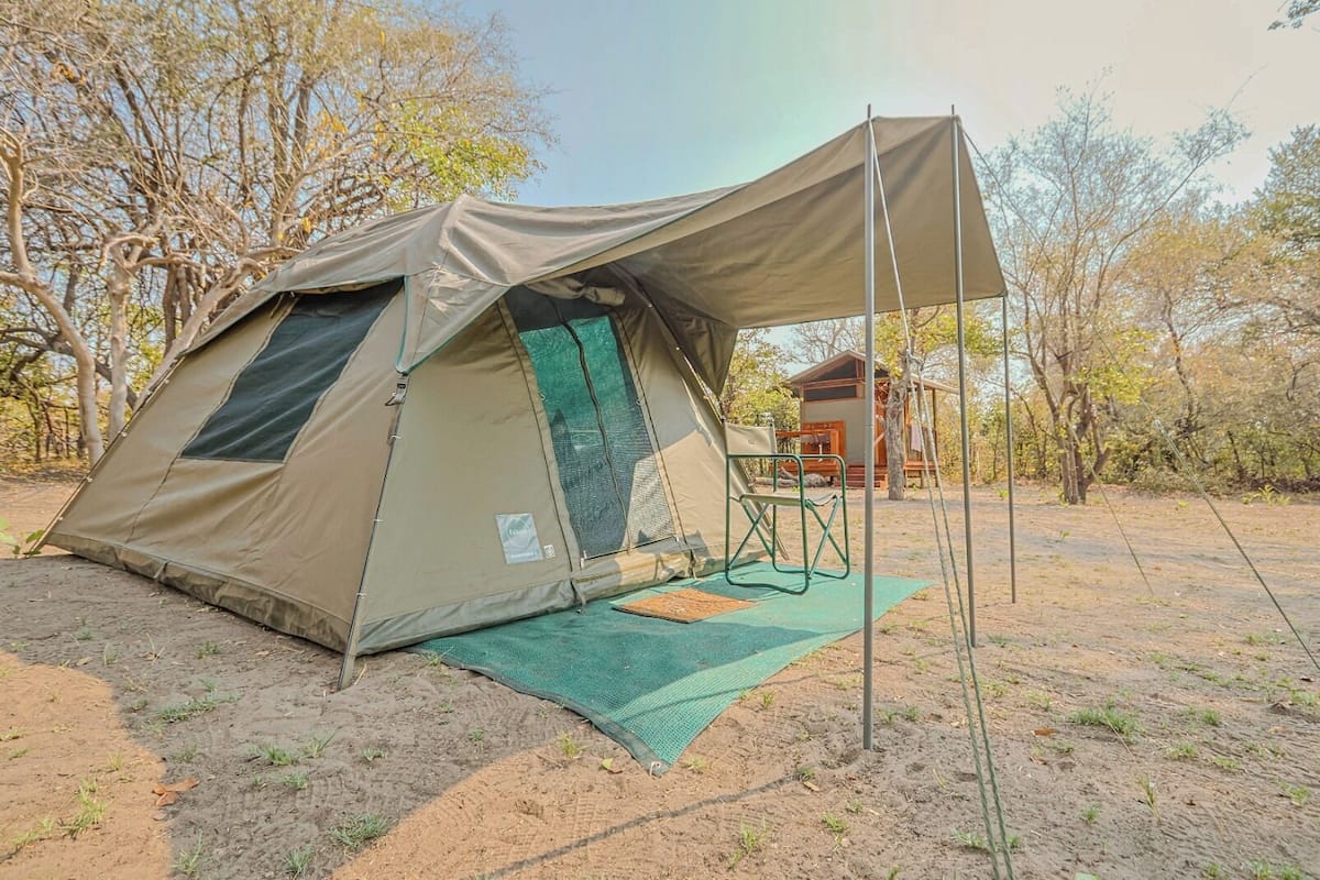 A large, beige tent with a mesh window and a green mat in front.