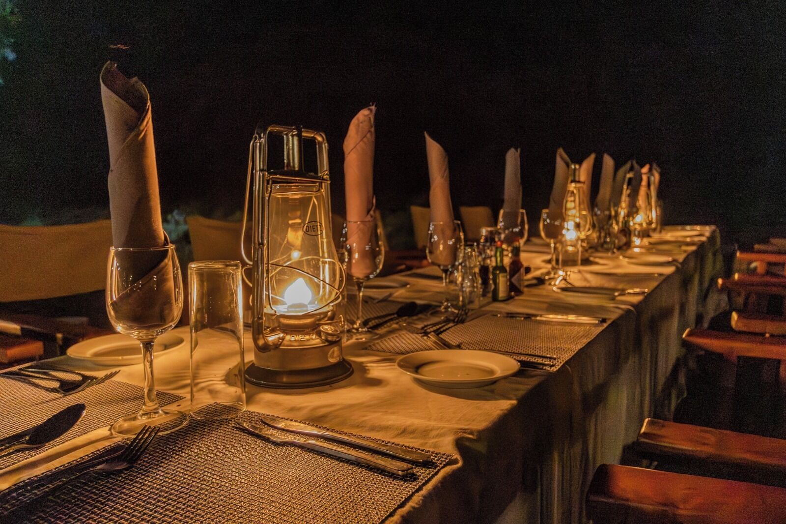 A long dining table set for a meal with candles, a lantern, and a warm ambiance.