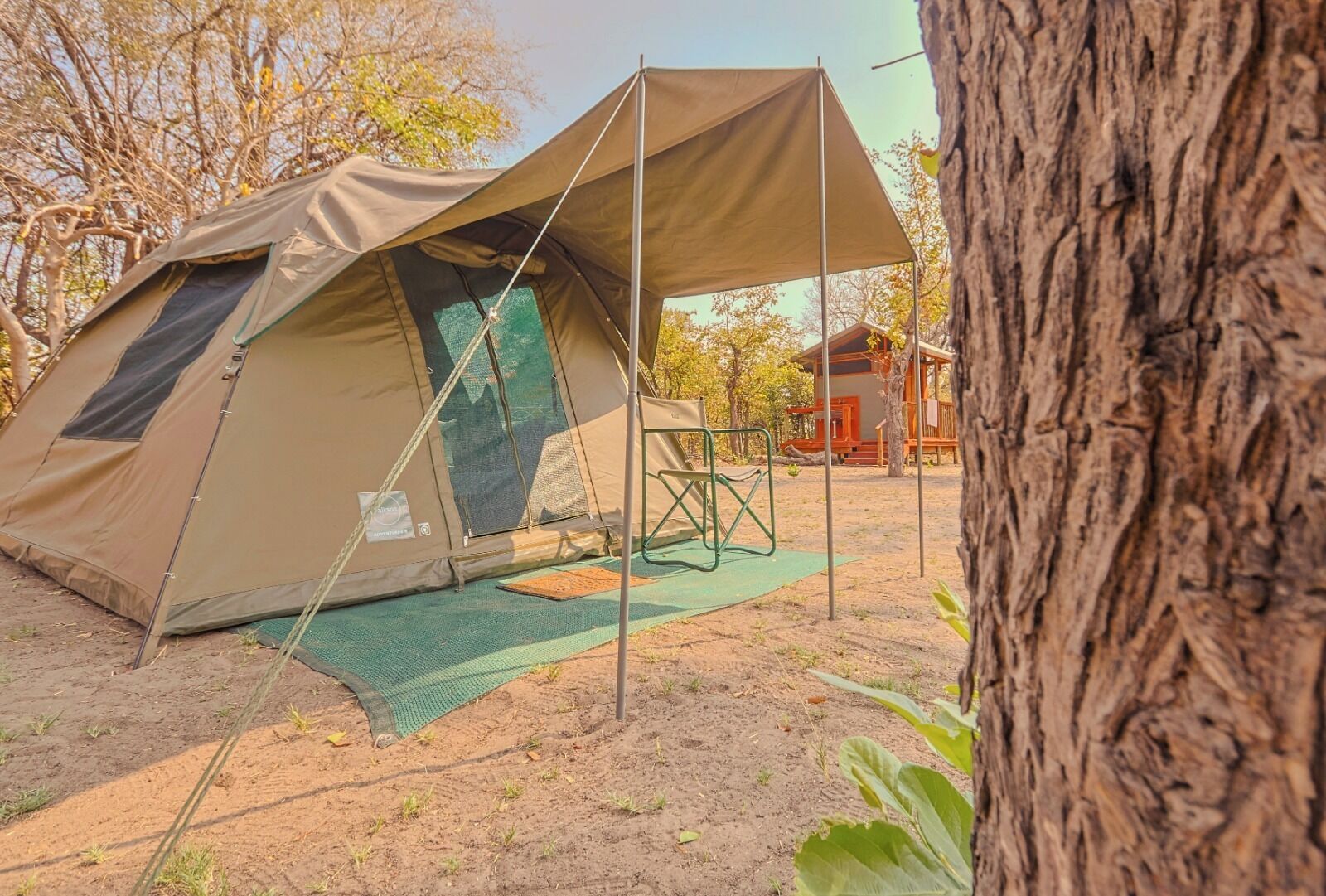 Uma tenda com um toldo, um tapete verde e uma cadeira.
