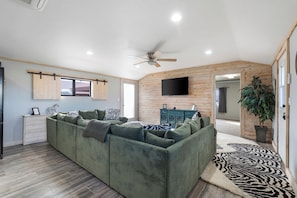 Una sala de estar moderna con un sofá modular, un ventilador de techo, un televisor montado y una pared de acento de madera.