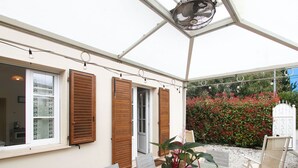 An outdoor patio with a table and chairs, a fan, and a view of a garden with red flowers.