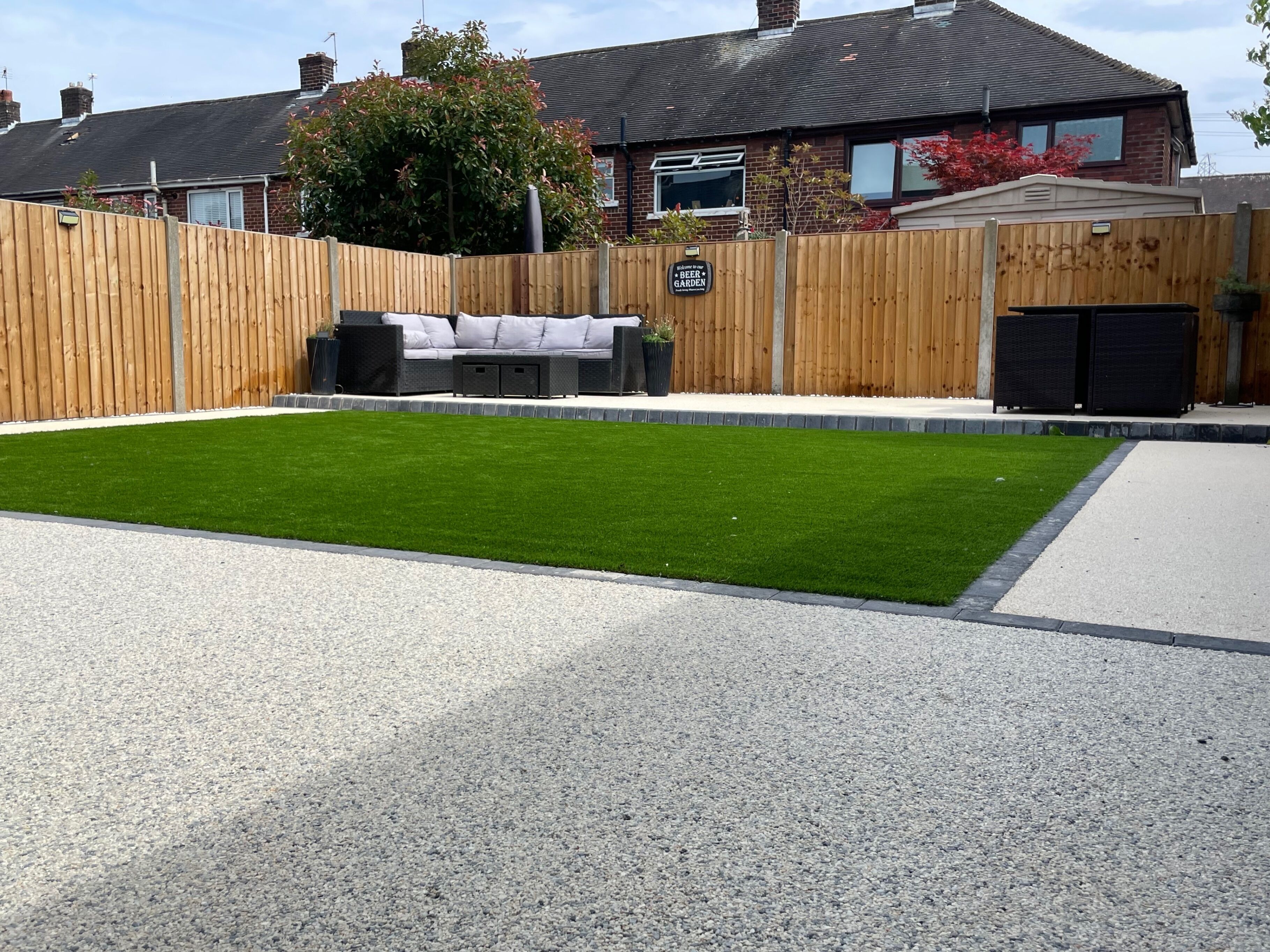 A backyard with a well-maintained lawn, a wooden fence, and a seating area with a sofa and table.