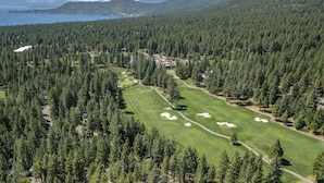 An aerial view of a golf course surrounded by dense forests and a mountain range in the background.
