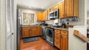 A kitchen with wooden cabinets, stainless steel appliances, and a window with blinds.