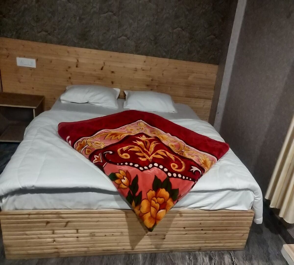 A bed with a wooden headboard, white bedding, and a decorative red and orange floral throw blanket.