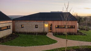 A modern house with a stone facade, a wooden extension, and a curved driveway.