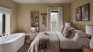 A bedroom with a large bed, a bathtub, and a window with curtains.