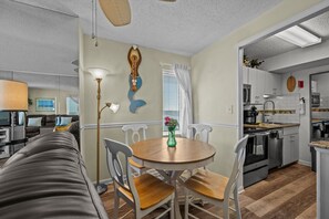 A cozy living room with a sofa, a dining table with chairs, a floor lamp, and a decorative wall piece. - Oceanfront Beach Condo, Pool, Gym, Fishing Surfing (Virginia Beach)