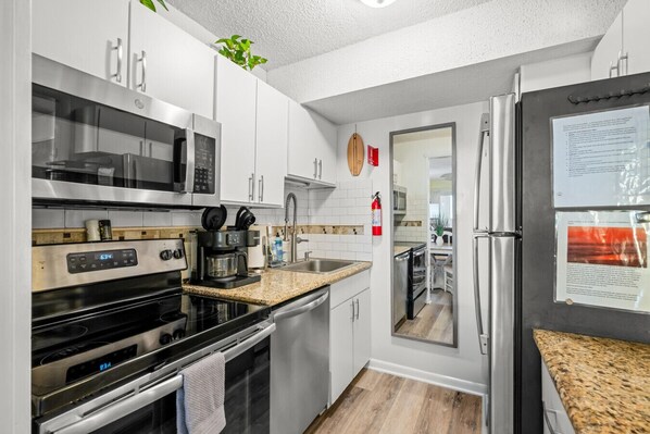 A modern kitchen with stainless steel appliances, white cabinets, and a granite countertop. - Oceanfront Beach Condo, Pool, Gym, Fishing Surfing (Virginia Beach)