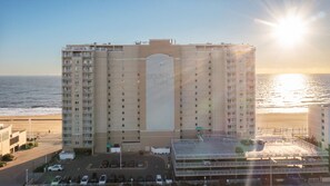 A multi-story hotel with a central entrance and a parking lot in front. - Oceanfront Beach Condo, Pool, Gym, Fishing Surfing (Virginia Beach)