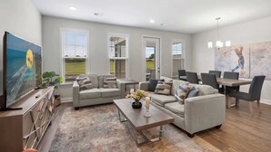Ein geräumiges Wohnzimmer mit einem großen Flachbildfernseher, grauen Sofas, einem Couchtisch und einem Essbereich mit Tisch und Stühlen.