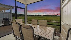 Ein überdachter Patio mit Tisch und Stühlen mit Blick auf einen Golfplatz bei Sonnenuntergang.